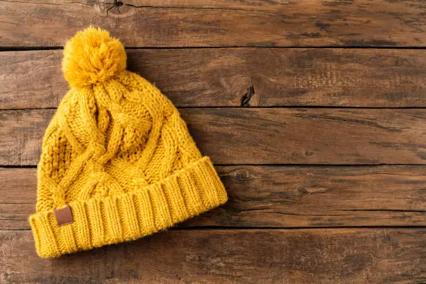 Yellow knitted hat on wooden background with copyspace. Top view