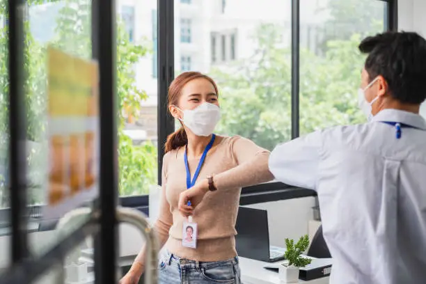 Photo of Asian businessman greeting with elbow bump or shaking elbow in working office to avoid touching due to infection of coronavirus covid-19, new normal life and social distancing concept