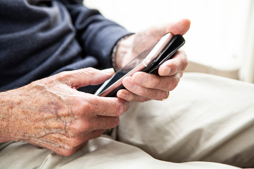 Close-up of an old person's hands holding a smartphone at home