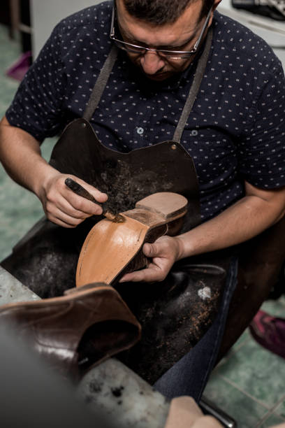 Cobbler repairing shoes Male cobbler sitting at his shop and repairing man's shoe, brushing glue over sole. Vintage look. cobbler dessert stock pictures, royalty-free photos & images