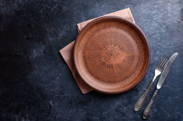 istock Round brown plate, for food, fork, knife, towel, on a dark background. Flat lay 1257250672