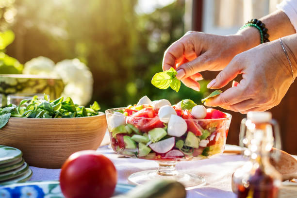 donna che mette foglia di basilico all'insalata di verdure - caprese salad foto e immagini stock