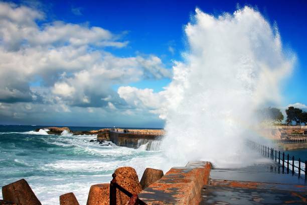 Waves breaking on the wall of a sea pool in Kalk Bay, South Africa, with mountains visible across the bay