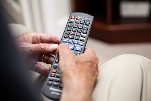 Close-up of an old person's hands pressing buttons on a TV remote at home