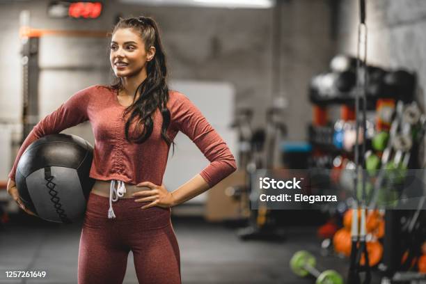Portrait Of Young Woman Lifting Medicine Ball In Fitness Center Strong Athlete Doing Cross Training At Gym A Woman Is Lifting A Weighted Ball At The Gym Stock Photo - Download Image Now