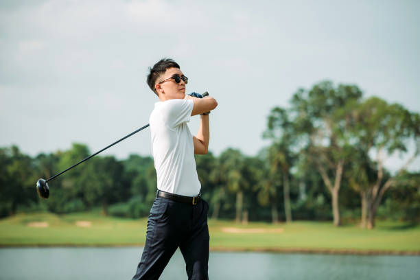 jeune golfeur chinois asiatique mâle avec des lunettes de soleil jouant au golf sur le terrain de golf - golf golf course swinging isolated photos et images de collection