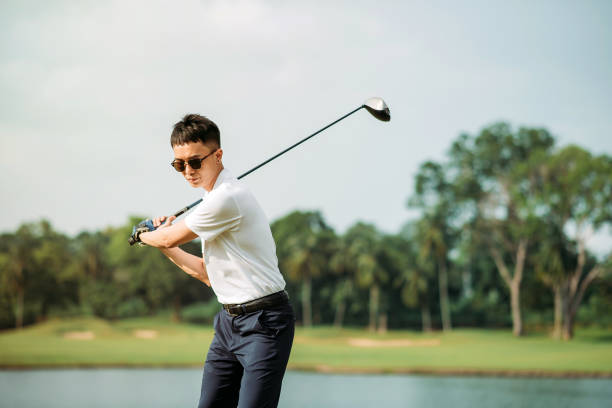 jeune golfeur chinois asiatique mâle avec des lunettes de soleil jouant au golf sur le terrain de golf - golf golf course swinging isolated photos et images de collection