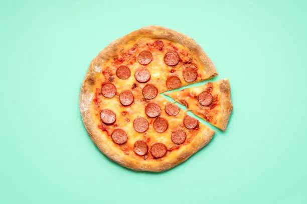 Flat lay with a pepperoni pizza on a green mint background. Single slice of pizza pepperoni top view. Homemade pizza with mozzarella, sausage and tomato sauce