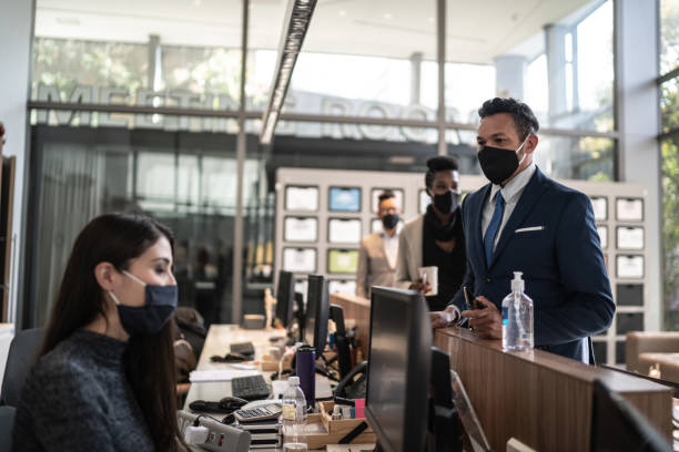 Businessman talking to receptionist on entrance of office's lobby - with face mask Businessman talking to receptionist on entrance of office's lobby - with face mask hotel reception hotel business lobby stock pictures, royalty-free photos & images