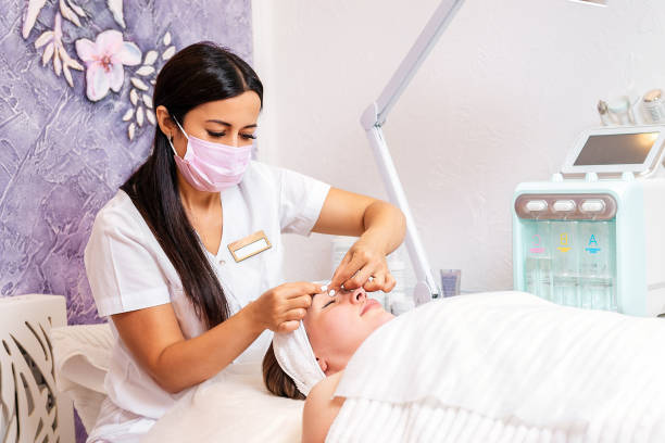 A cosmetologist in a medical mask does a facial massage procedure for a client. The concept of cosmetology during the viral pandemic A cosmetologist in a medical mask does a facial massage procedure for a client. The concept of cosmetology during the viral pandemic. beautician stock pictures, royalty-free photos & images
