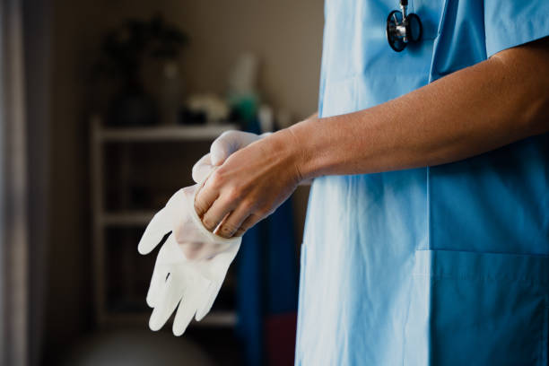 Close up of Female doctor in scrubs putting surgeon gloves on hands Close up of caucasian female doctor in scrubs putting surgeon gloves on hands. High quality photo putting on latex gloves stock pictures, royalty-free photos & images