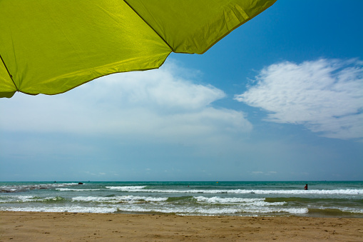 Bottom of an umbrella on the shore of the beach with waves and the sea and the blue sky and some clouds in the background. Summer, vacation or safety concepts