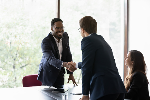Mixed race and Caucasian business partners start group meeting shake hands express regard. Happy candidate get hired job interview accomplish. Gesture of approval acceptance, business promises concept