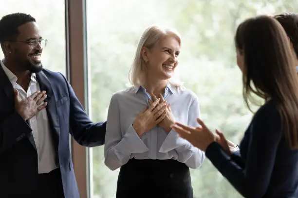 Photo of Middle-aged businesswoman get congrats and compliments from multiethnic colleagues