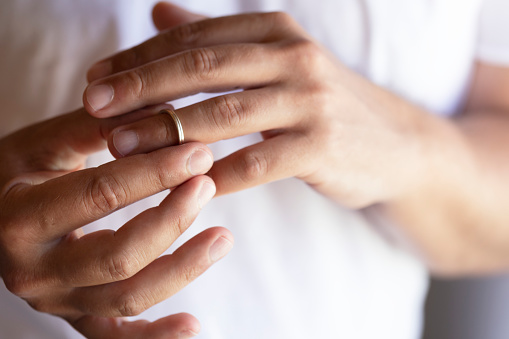 Hands of caucasian male wearing white t-shirt  who is about to taking off his wedding ring.
