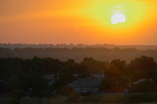 The white sun in the orange sunset of the evening haze above the village.