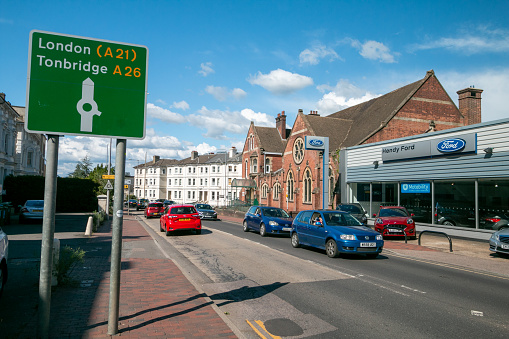 Royal Tunbridge Wells in Kent, England, with a road sign pointing to London and Tonbridge, and number plates visible in the background. Ford garage is in the background.