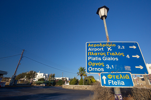 Mykonos Road Sign in The Cyclades, Greece, with directions to the airport, Platis Gialos, Ormos and Ftelia. Gas station details can be seen in the background as well as designs on the wall.