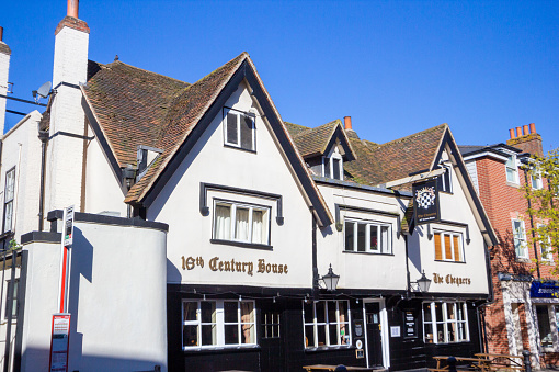 The 16th century house on Sevenoaks High Street is known as The Chequers and is a popular pub. Other shops' names and logos are visible as well as the pub's coat of arms.