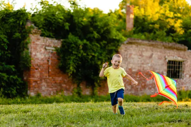 Photo of Funny excited boy running on a meadow while playing with a rainbow kite