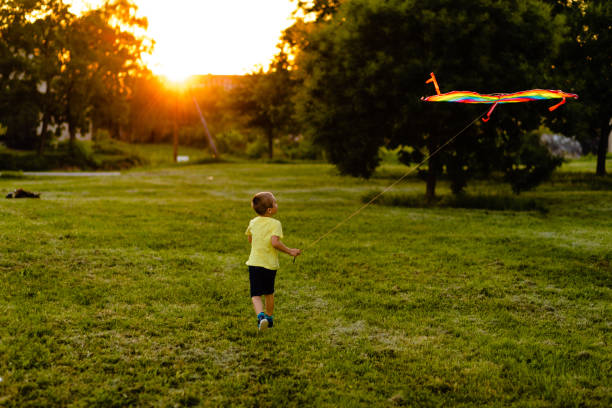 istock Funny boy enjoying summer day while playing with a rainbow kite in sunset 1257277018
