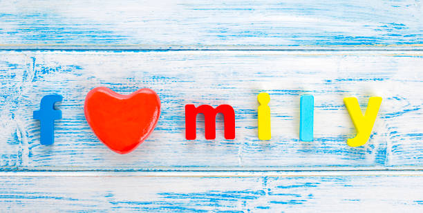 The word "Family", made of multi-colored wooden letters. The word "Family", made of multi-colored wooden letters and a red heart on a painted wooden background. Happy family concept. Children training. Copy space. Flat lay. family word stock pictures, royalty-free photos & images