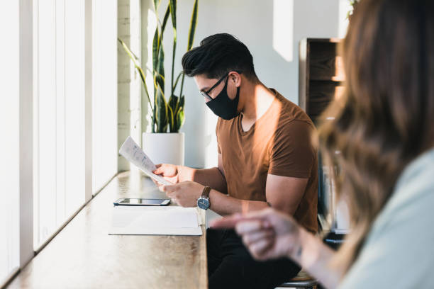 istock Man wearing protective mask reviews data for unrecognizable co-worker 1257278514
