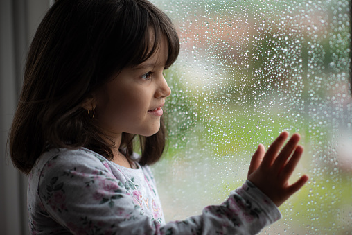 a 5 years old girl looking at rain out of the window.