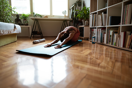 High angle view of a young Caucasian woman doing yoga at home.  Working on stretching, strength, and body balance. Practicing meditation and breathing exercises at home.