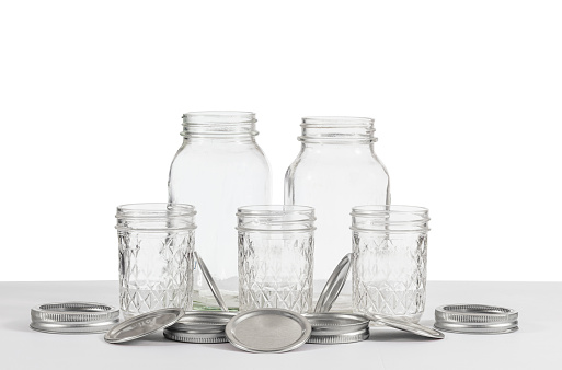 Horizontal shot of a group of old canning jars of two different sizes with rings and lids on a white background.