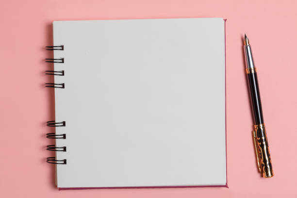 istock Top view of a blank notepad next to a pen on a pink background. 1257290615