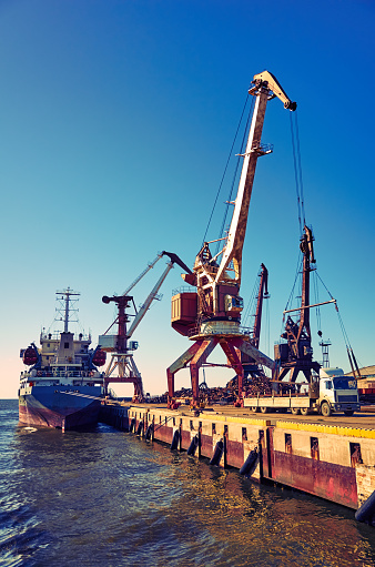 Cargo ship docked pier unloading freight with cranes, sea and blue sky, vibrant color