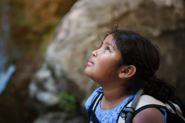 Young girl with hiking backpack looks up towards a difficult hiking trail ahead of her. stock photo