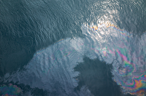 Oil slick on the sea surface. Ripple of blue water, sunlight reflected