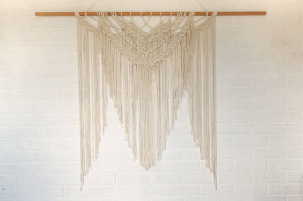 Beige reed against a white wall with a macrame wall panel. A minimal, stylish, trendy concept with a beautiful background with light neutral colors.
