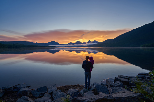 Father and daughter looking at a vibrant sunrise in the beautiful natural scenery of Glacier National Park's Lake McDonald area in Montana, USA.