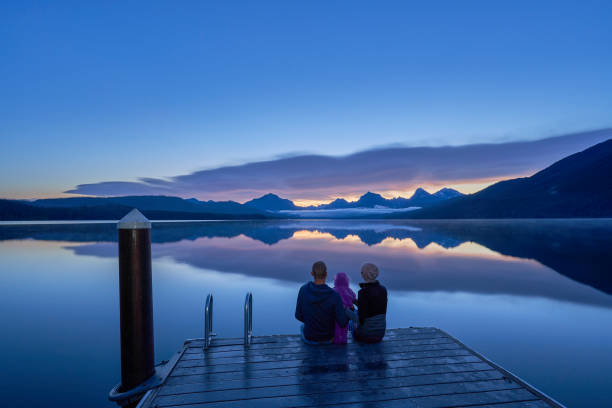 family take in a vibrant sunrise in the beautiful natural scenery of glacier national park's lake mcdonald area during the summer in montana, usa. - montana mountain mcdonald lake us glacier national park imagens e fotografias de stock