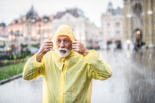 Senior man in raincoat walking in rain.