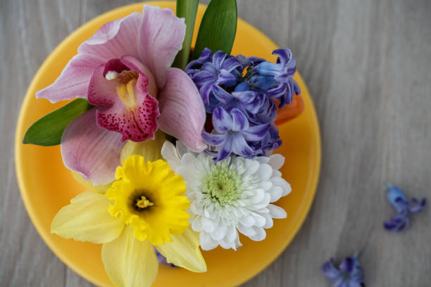 Close up shot of abundance of different colorful, spring flowers arranged in a bouquet in a tea cup and put on a wooden table as a decoration.