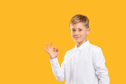 OK gesture. Deal agreement. Confident boy smiling showing approval hand signal isolated on orange copy space.
