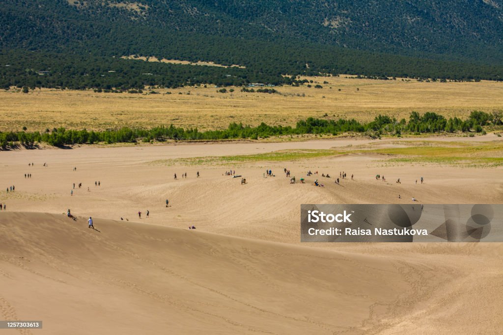 Groups of tourist hikers walk on giant desert sand dunes surrounded by mountains at the Great Sand Dunes National Park in Alamosa, Colorado, USA Tourists hike and play on giant sand dunes Colorado Stock Photo