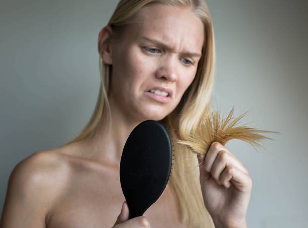 Worried woman looking at her split ends in the bathroom. Hair damage. A pretty blonde woman standing in the bathroom holding her dry split ends of hair making a unhappy face. human hair women brushing beauty stock pictures, royalty-free photos & images