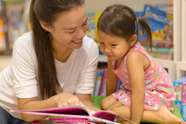 mãe lendo um livro de história para seu filho na biblioteca. crianças aprendendo a ler. - picture book library preschool bookshelf - fotografias e filmes do acervo