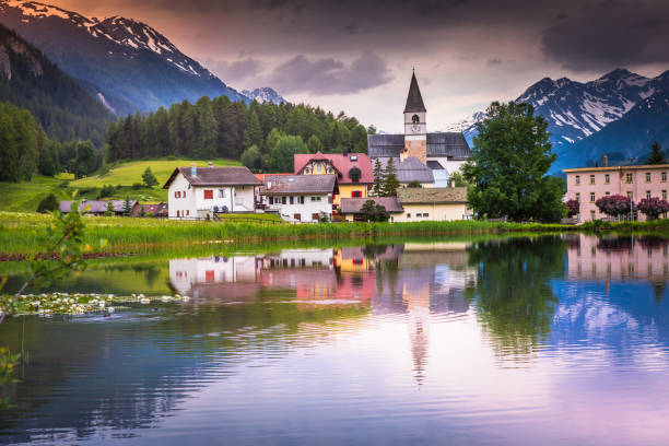 идиллический пейзаж - церковь, полевые цветы и отражение озера в деревне тарасп, энгадин - швейцария - mountain switzerland scuol mountain peak стоковые фото и изображения