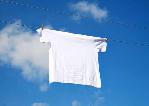 Closeup of a single white shirt on a clothesline in the sunshine.