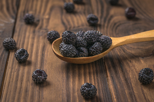 Black raspberries in a wooden spoon and on the table. Freshly harvested berries.