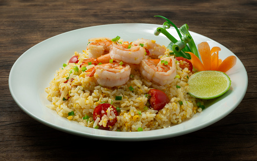 Fried Rice with Shrimps and tomatoesThai Food popular dish of Asian decorate carved Spring onion and lime Wood Background sideview