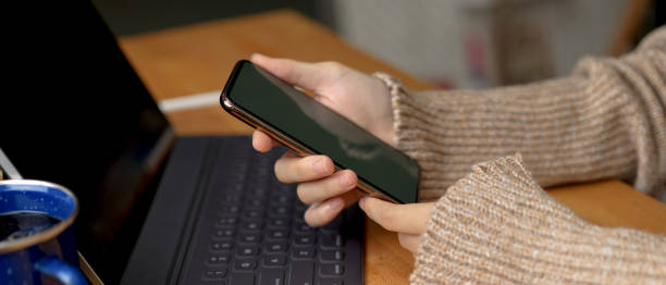 istock Female hands holding smartphone while sitting at workspace with digital tablet on wooden table 1257321529