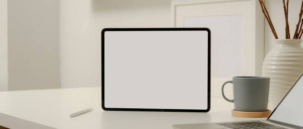 istock Blank screen tablet on white worktable with stylus pencil, laptop, coffee cup and decoration 1257322600