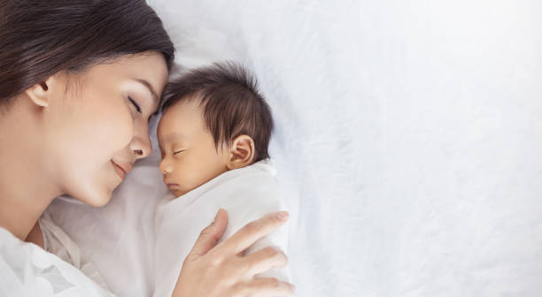 close up portrait of beautiful young asian or caucasian mother girl kissing her healthy newborn baby sleep in bed with copy space. healthcare and medical love asia woman lifestyle mother's day concept - baby imagens e fotografias de stock